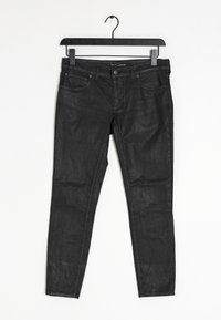 Jeans de mezclilla negra con un ajuste slim, que cuentan con bolsillos frontales, costuras decorativas y una textura suave. Se cuelga de una percha de plástico negro.