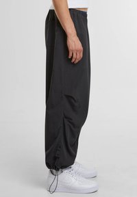 Zwarte nylon joggers met een elastische tailleband, zijzakken en verstelbare manchetten. Gestyled met witte sneakers voor contrast.