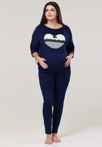 Námornícky modrý tehotenský outfit pozostávajúci z krátkopestrihatého trička s návrhom srdca a čipkovými akcentmi, v kombinácii s úzkymi nohavicami. Jemný materiál, voľný strih.