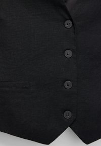 Chaleco de lino negro con cinco botones negros, un bolsillo en el pecho y un dobladillo inferior en punta. Textura suave, diseño simple.