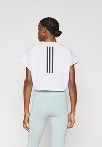 Λευκό κοντό T-shirt με φαρδιές μανίκια που έχει τρεις μαύρες κάθετες ρίγες στην πλάτη, σε συνδυασμό με στενά ανοιχτό μπλε κολάν.