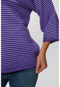 Fialový proužkovaný top z žebrované pleteniny, s širokými rukávy a přiléhavým střihem, kombinovaný s modrými džínami.