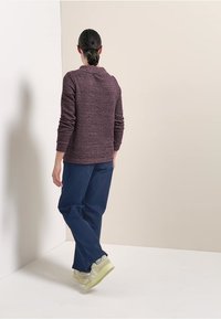 Bordowy sweter o fakturze z wysokim kołnierzem, w połączeniu z granatowymi spodniami i jasnymi sneakersami. Model odwrócony plecami do aparatu.