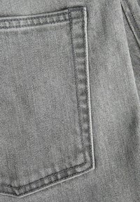 Harmaa denim-kangas, jossa on lähikuva takataskusta, jossa on erottuva ommel ja siisti, rakennettu suorakulmainen muoto.
