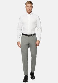 Witte langemouwenshirt met een spredkraag, grijs geruite broek, zwarte leren riem en bijpassende zwarte geklede schoenen.