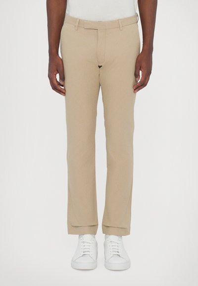 Beige bomuldsbukser med slim fit, med en taljeværd, forlommer og oprullede cuffs, parret med hvide sneakers.