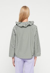 Zielono-biała koszula w kratkę gingham z falbanianym kołnierzykiem, długimi rękawami i luźnym fasonem, prezentowana na modelce widzianej od tyłu.