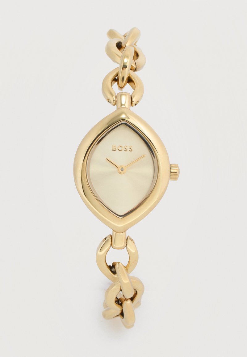 Χρυσό ρολόι χειρός με καντράν σε σχήμα φύλλου, μινιμαλιστικό καντράν που δείχνει 2:10, μπρασελέ με αλυσίδα και το κείμενο "BOSS" στο καντράν.