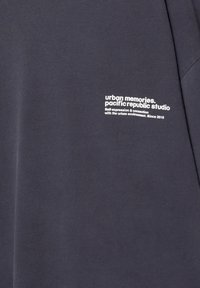 Mørkegrå stof med en teksttryk i hvid, der beskriver "urbane minder. pacific republic studio" med yderligere tekst nedenfor.