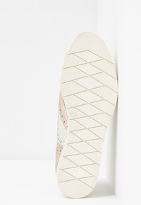 Baskets en daim beige et panneaux en cuir blanc, dotées d'une semelle extérieure en caoutchouc texturé avec un motif de crampons en losange et une indication de taille.