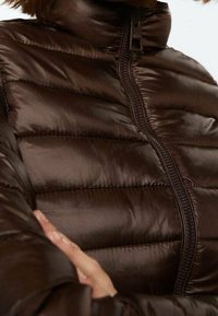 Brown puffer jacket featuring a high collar, horizontal quilted pattern, and a central zipper closure, made from a glossy, smooth fabric.