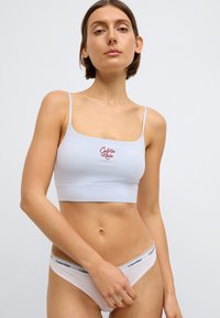 Ανοιχτό γαλάζιο σουτιέν bralette με λεπτές τιράντες και κόκκινο λογότυπο "Calvin Klein". Λευκά βρακάκια με μαύρη μέση και λογότυπο. Μαλακό, ελα�στικό υλικό.