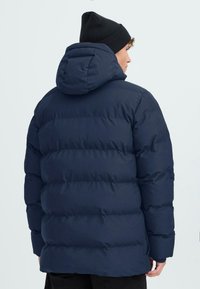 Námořnická pufovaná bunda s hustým prošívaným designem a kapucí. Vyrobena z hladkého materiálu, má volný střih a elastické manžety.