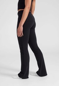 Zwarte flared leggings van rekbare stof, met een hoge tailleband en een gladde textuur, gecombineerd met witte sokken.