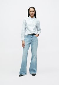 Jasnoniebieska koszula w paski z długim rękawem, o luźnym kroju, zestawiona z rozkloszowanymi, jasnoniebieskimi dżinsami i czarnymi butami na spiczastym nosku. Prosty design, casualowy wygląd.