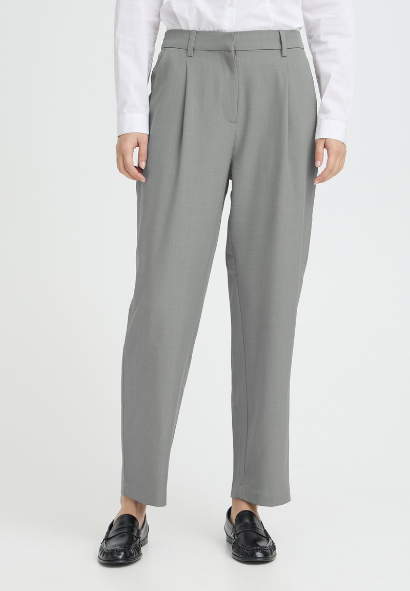 Pantalon gris sur mesure à coupe droite, avec deux plis avant et passants pour ceinture, associé à des mocassins noirs. Texture de tissu lisse.