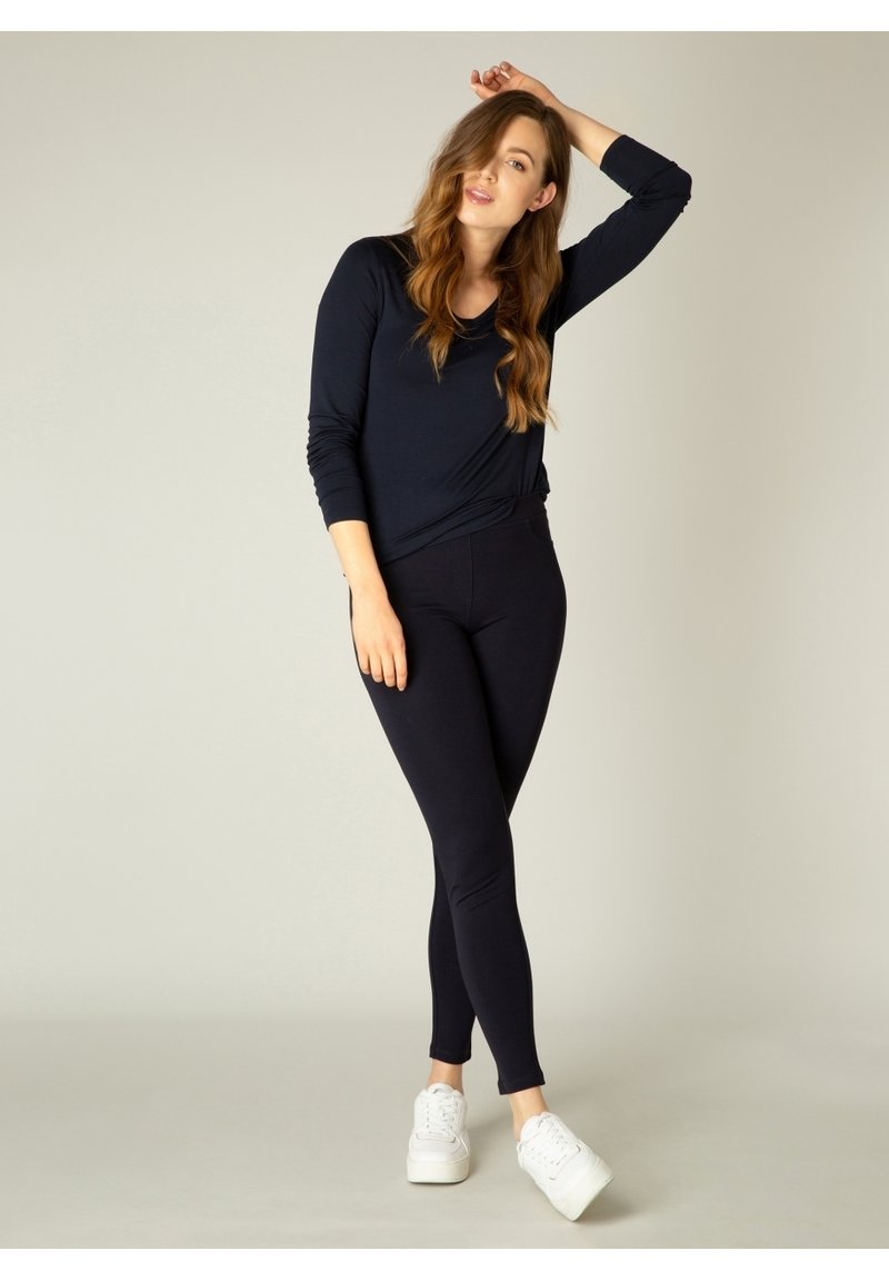 Marineblauw langslobtop, getailleerde zwarte leggings en witte sneakers. De top heeft een ronde halslijn en de leggings hebben een gladde textuur.