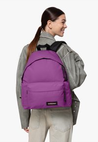 Mochila Eastpak morada con una textura suave, bolsillo frontal y correas ajustables. Detallada con herrajes y logo en negro.