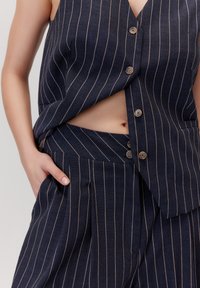 Morska, w paski, dwuczęściowa stylizacja składająca się z bezrękawowej bluzki z dekoltem w serek oraz guzikami, połączona z spodniami z wysokim stanem, uszytymi z fakturowanej tkaniny.
