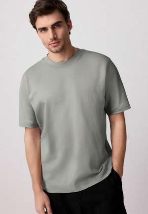 Tricou gri deschis, cu guler rotund, fabricat dintr-un material moale. Mâneci scurte, croială lejeră, design minimalist fără modele sau accente vizibile.