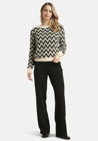 Black and cream zigzag patterned sweater in soft, fuzzy fabric, paired with sleek black pants. The sweater has a wide crew neck and ribbed cuffs.