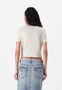 Pjūvis, trumpa rankovė t-shirt švytinčio šviesiai rudo audinio. Turi apvalią iškirptę, lygų paviršių ir derinama su aukštu juosmeniu mėlynais džinsais.