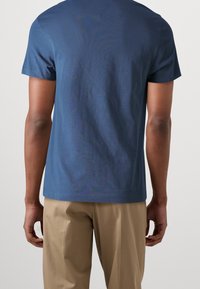 Blue cotton t-shirt with short sleeves and a v-neck, featuring a soft texture and a relaxed fit, paired with beige trousers.