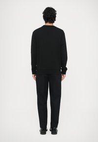 Czarna bluza o luźnym kroju i długich rękawach, zestawiona z czarnymi, dopasowanymi spodniami i czarnymi butami, widziana od tyłu.