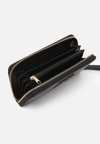 Svart lærwallet med glidelås rundt design, som har flere kortlommer og en sentral glidelåsrom. Gullfargede metall-detaljer.