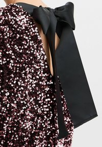 Paljettklänning med en mörk burgunder, texturerad yta. Har en stor svart satinrosett vid halsringningen, med en öppen ryggdesign.
