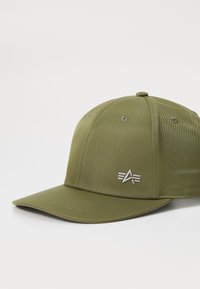 Oliven grøn baseballcap lavet af tekstureret stof, med en buet skygge og en sølvfarvet logoaccent på forsiden, samt ventilationshuller.