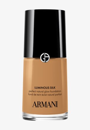 Luminous Silk foundation i en elegant glassflaske. Brun væske med sort kork som har en logo. Tekst på flasken inkluderer produktdetaljer.