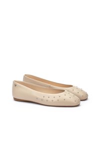 Bailarinas de piel beige con puntera redondeada, decoradas con pequeñas tachuelas plateadas, que presentan una textura suave y suelas de goma flexibles.