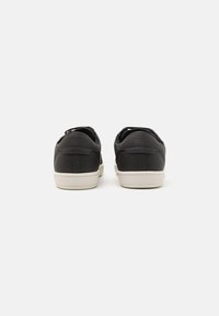 Ein Paar schwarze Low-Top-Sneaker mit weißen Sohlen, von hinten auf einem schlichten hellen Hintergrund gezeigt.