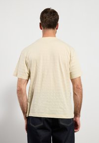 Camiseta de color beige claro con mangas cortas, que presenta una textura de rayas horizontales, fabricada con un tejido suave, combinada con unos jeans de mezclilla oscura.