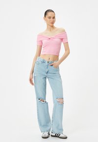 Ljusrosa ribbad crop-top med off-shoulder-design, kombinerad med ljusblå slitna vida jeans och grå sneakers med svarta ränder.