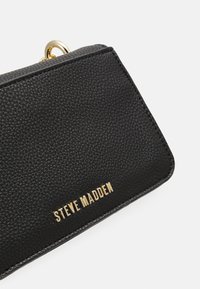 Svart texturerad plånbok med guldfärgade detaljer och präglad "STEVE MADDEN" logotyp på framsidan. Kompakt design med en modern estetik.