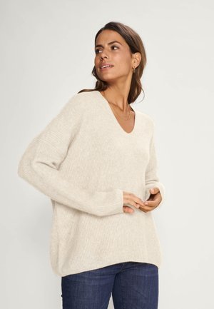 Cream-colored knitted sweater with a V-neck, drop shoulders, and long sleeves. Features a relaxed fit and ribbed texture.