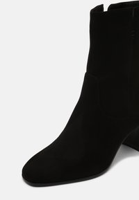 Czarne zamszowe botki za kostkę z wąskim noskiem i lekko wygiętym obcasem. Gładka textura z minimalnymi akcentami i detalami przeszyć.