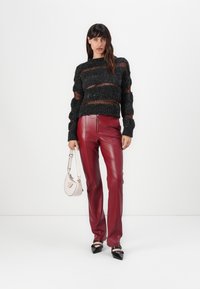 Black knitted sweater with horizontal orange stripes, paired with fitted red leather pants. Accessorized with a small cream handbag and black heels.
