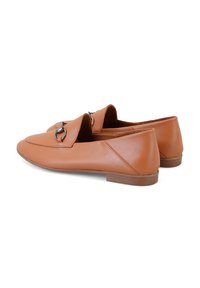 Hellbraune Lederloafers mit runder Zehenform, die ein dekoratives Detail aus silberfarbenem Metall und einen niedrigen, flachen Absatz aufweisen. Glatte Textur.