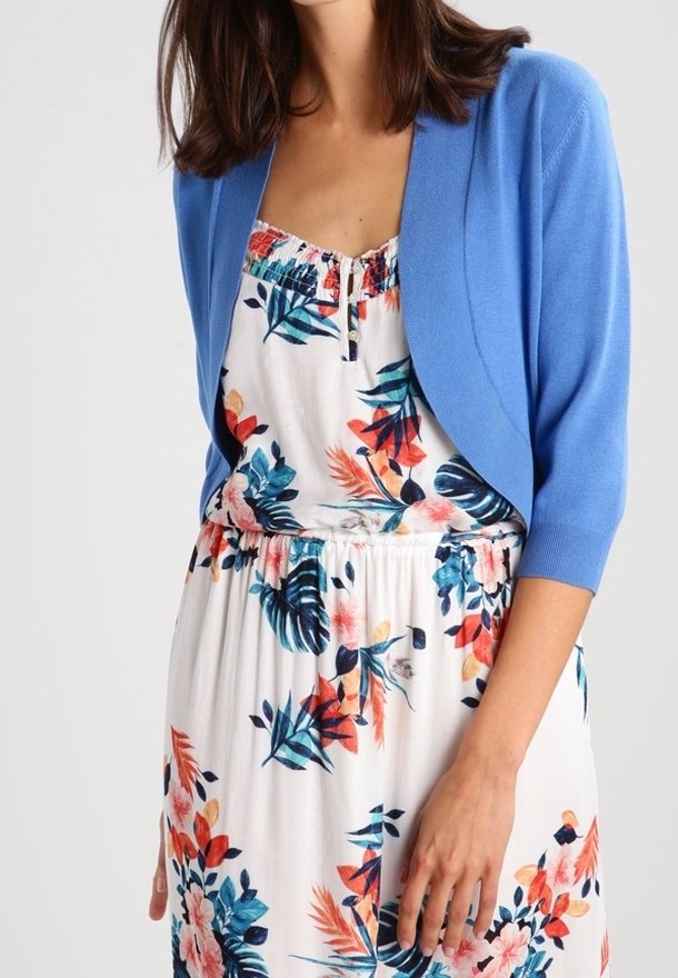 Light blue cardigan featuring a cropped design with three-quarter sleeves, worn over a white floral patterned dress with colorful accents.