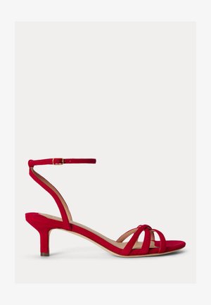 Κόκκινο σουέτ σανδάλι με χαμηλό τακούνι, λεπτό λουράκι στον αστράγαλο, ανοιχτή μύτη και τρεις λεπτές μπροστινές λουρίδες σε λευκό φόντο.