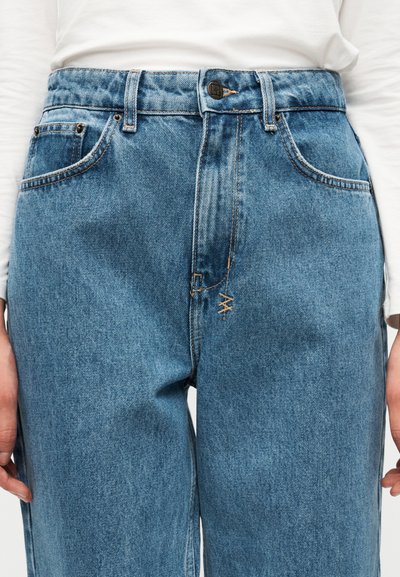 Ανοιχτό μπλε τζιν παντελόνι με ψηλή μέση, πέντε τσέπες και εμφανείς ραφές. Το υλικό φαίνεται με υφή και ελαφρώς ξεθωριασμένο φινίρισμα.