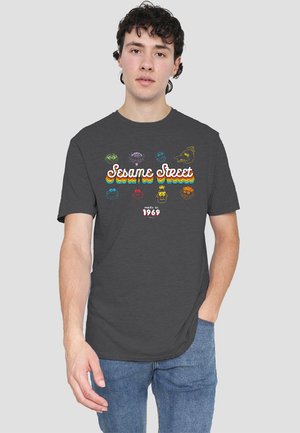 Dark gray t-shirt featuring a colorful "Sesame Street" graphic with character faces and rainbow stripes. Cotton blend, relaxed fit.