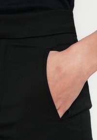 Czarne spodnie z boczną kieszenią i gładkim, teksturowanym materiałem. Szeroki pas zapewnia wygodne dopasowanie.