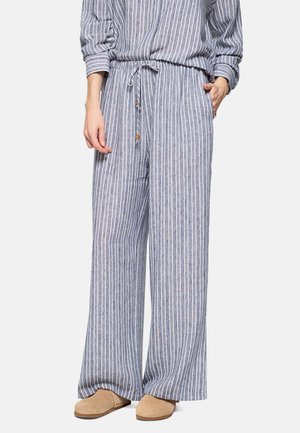 Mujer con pantalones de pierna ancha a rayas verticales azules y blancas, con cintura ajustable con cordón y zapatos beige sin cordones.