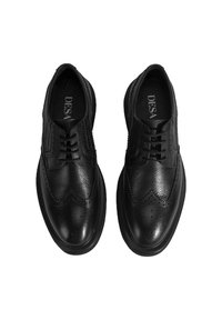 Schwarze Lederschuhe mit einem Wingtip-Design, strukturiertem Obermaterial, dekorativen Perforationen und einer dicken schwarzen Gummisohle.