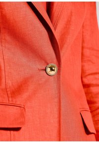 Rode linnen blazer met een visgraattextuur, gouden knoopdetails en twee voorzakken. Close-upweergave benadrukt het materiaal en het ontwerp.