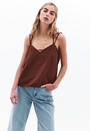 Top de tirantes finos texturizado en color marrón con un detalle en el escote, combinado con unos pantalones vaqueros de pierna ancha en azul claro.